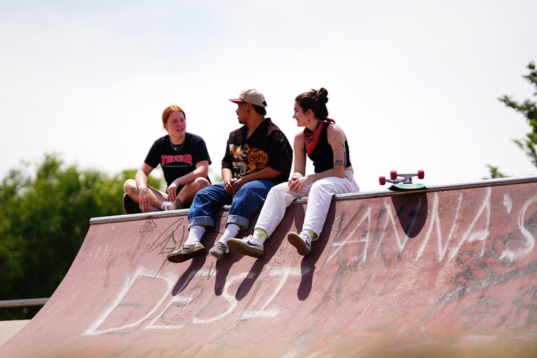 three skaters sitting at the top of a graffitied ramp