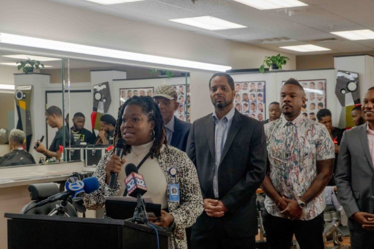 ANDREA HARVEY AT the podium in Walmart in front of (left to right) Larry E. Roberts Sr., Ald. Anthony A. Beale, Larry E. Roberts Jr., and Larry’s Barber College Chief Operating Officer, Adam Farmer.