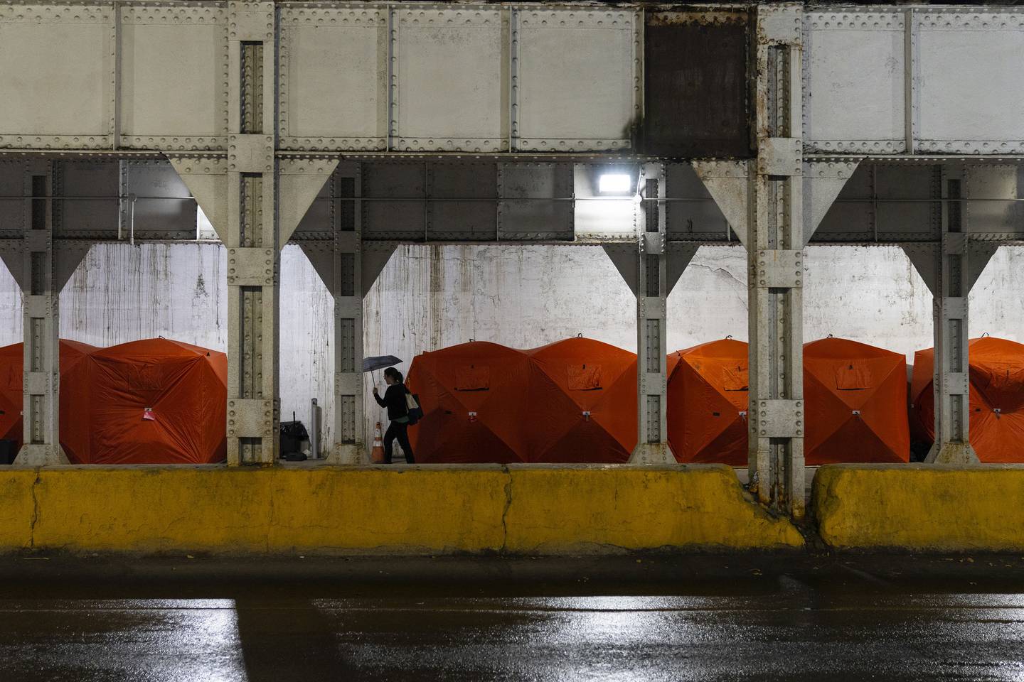 A pedestrian passes some of the ice-fishing shelters provided by an organization called Feeding People Through Plants over the weekend for unhoused people encamped under the Metra bridge on Milwaukee Avenue.