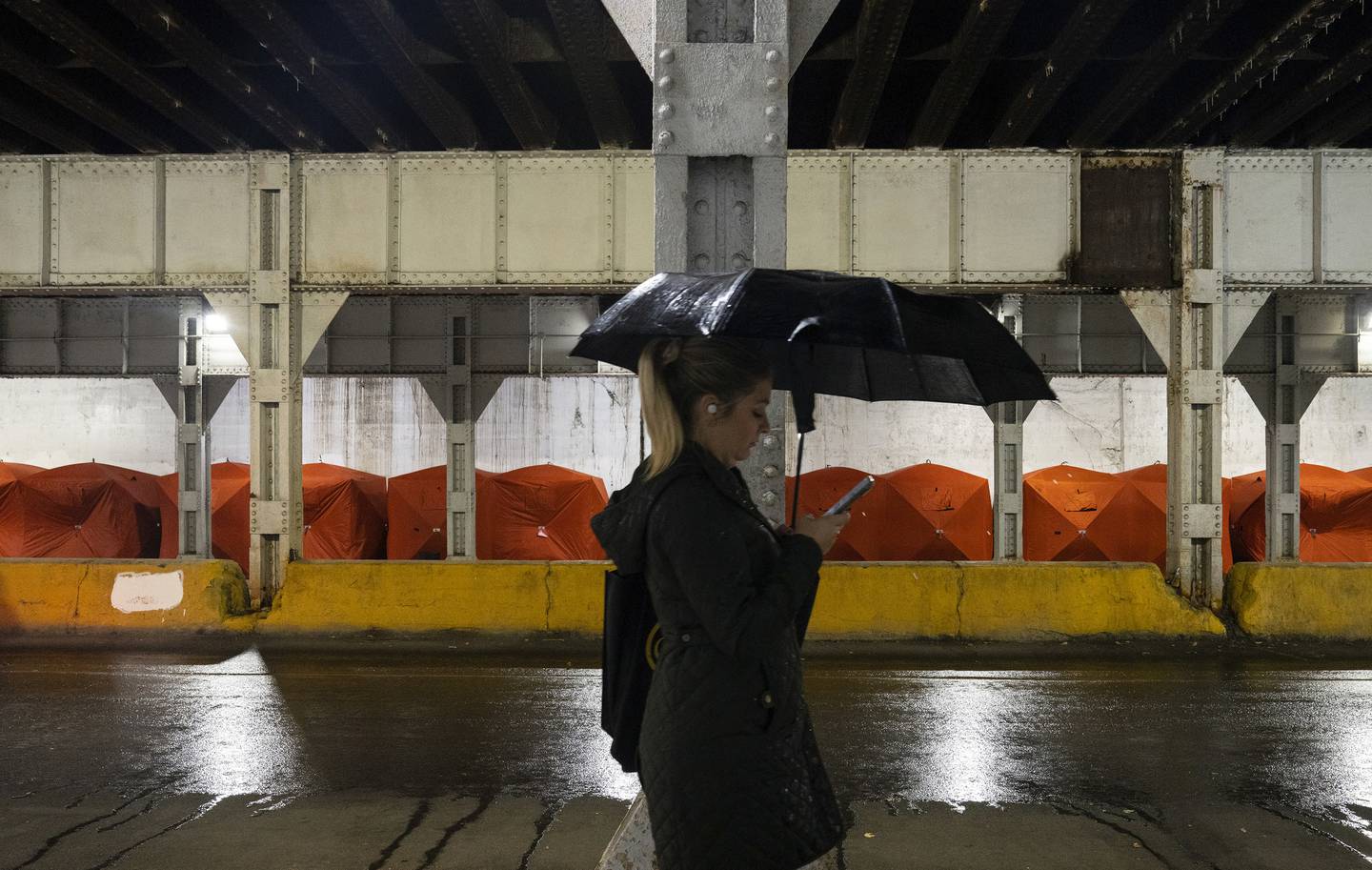 A pedestrian passes some of the winterized tents provided by an organization called Feeding People Through Plants over the weekend for unhoused people encamped under the Metra bridge on Milwaukee Avenue.