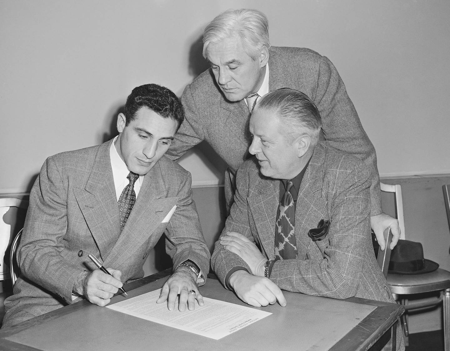 Charley Trippi, left, signs a four-year, $100,000 contract with the Chicago Cardinals on Jan. 17, 1947, in Chicago, as coach Jimmy Conzelman, center, and owner Charles Bidwell watch.