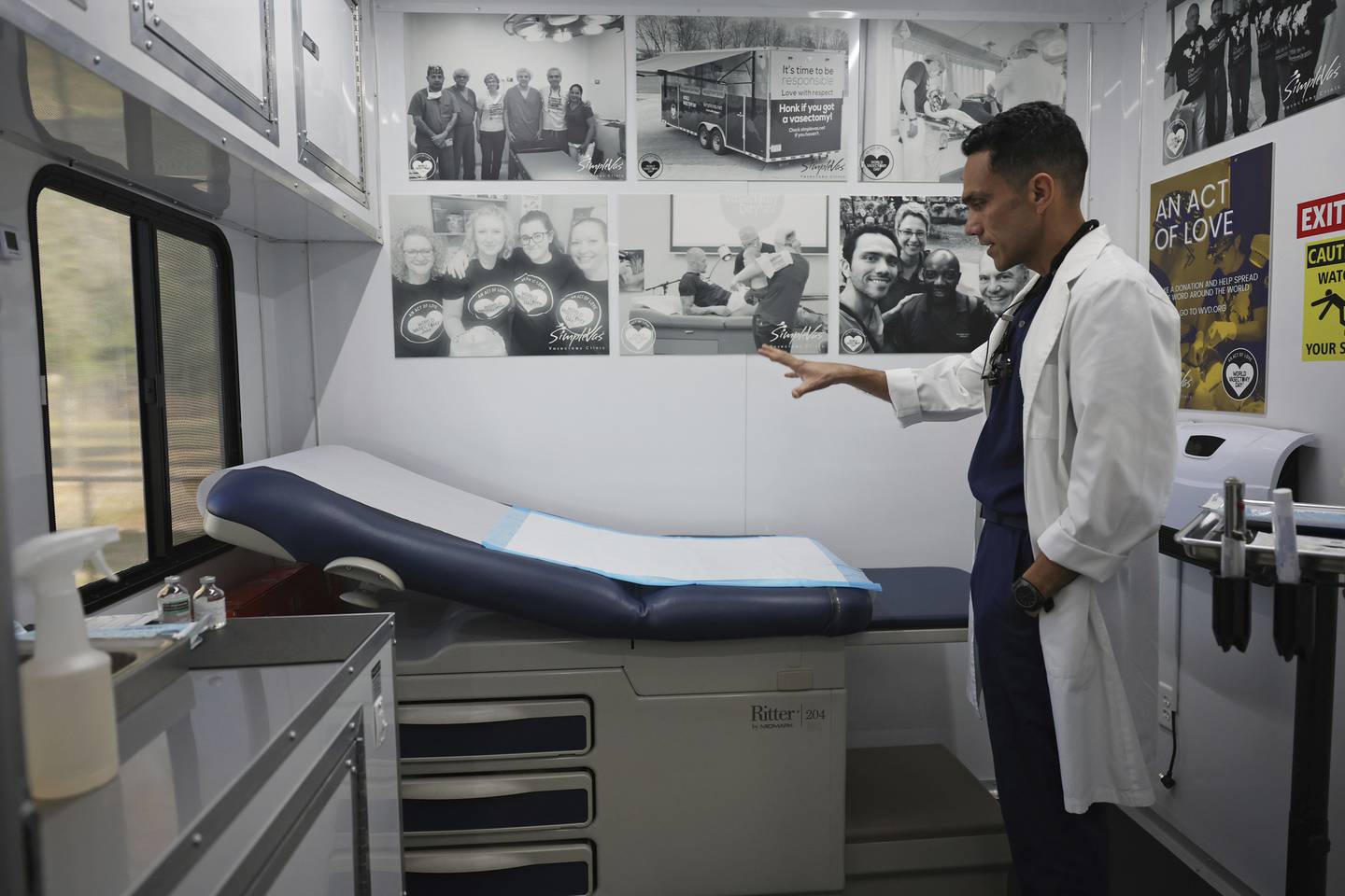 Dr. Esgar Guarín describes the equipment installed for providing vasectomies in his mobile medical clinic, parked at a community health clinic parking lot in Waterloo, Iowa. The trailer is decorated with photographs of himself with colleagues and patients involved in vasectomy procedures in domestic and international settings.