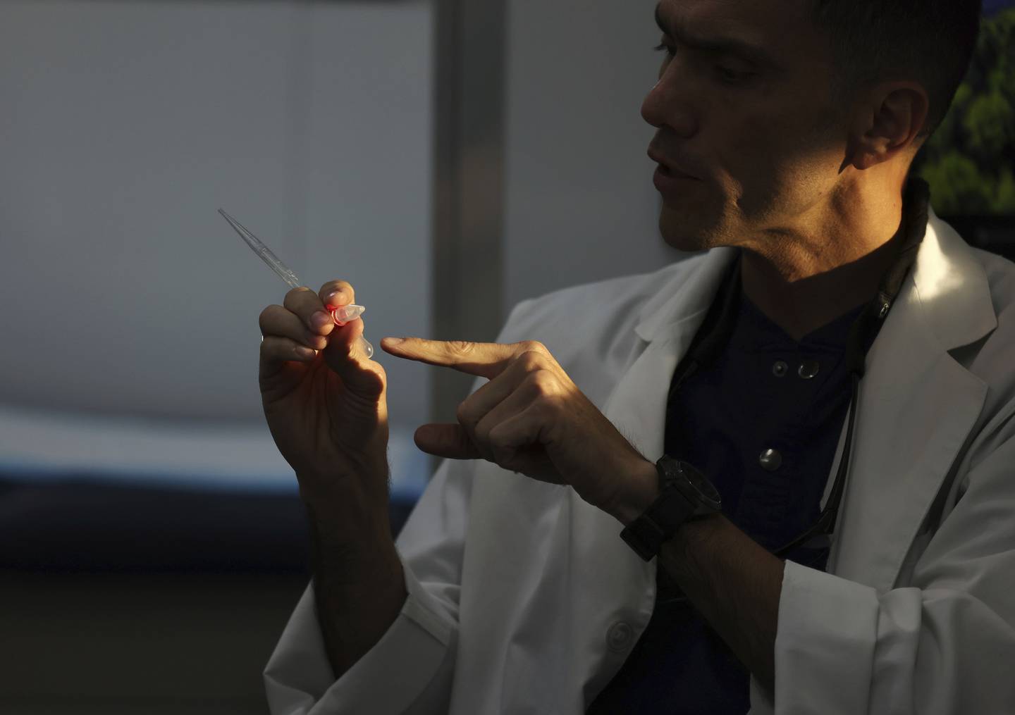 Late-afternoon sunlight shines on Dr. Esgar Guarín as he shows items from a post-procedure care box, including containers to send follow-up samples of semen, to a patient before performing a vasectomy in his mobile medical clinic.