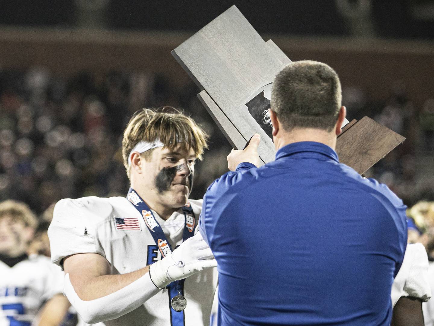 Lincoln-Way East's Jake Scianna (1) is handed the Class 8A state runner-up trophy at the University of Illinois' Memorial Stadium in Champaign on Saturday, Nov. 26, 2022.