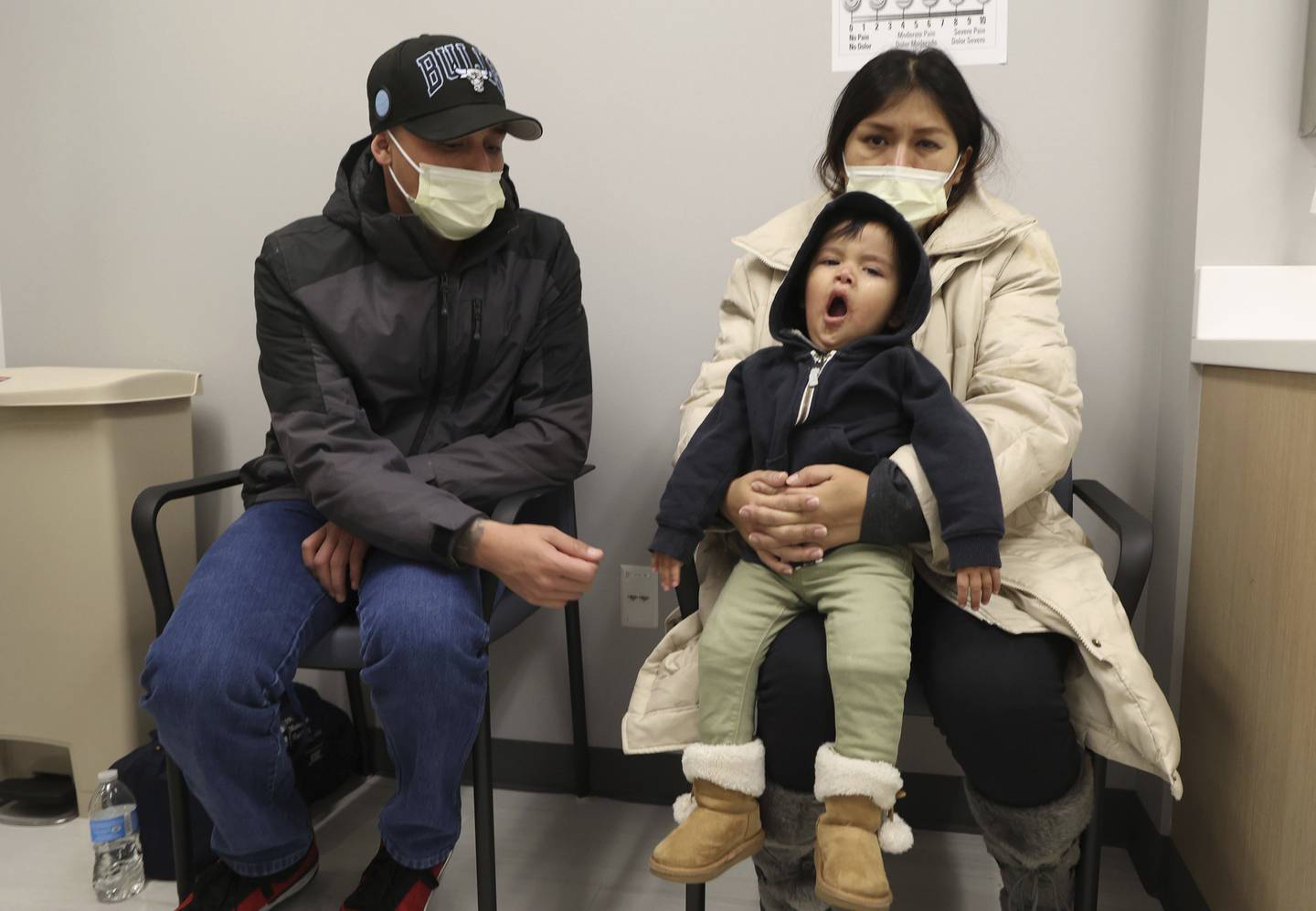 Silvia Gaby Calderon sits with her husband as their daughter yawns while waiting to be examined by a doctor at the Cook County Health Clinic in Chicago, Nov. 18, 2022. They are from Peru.