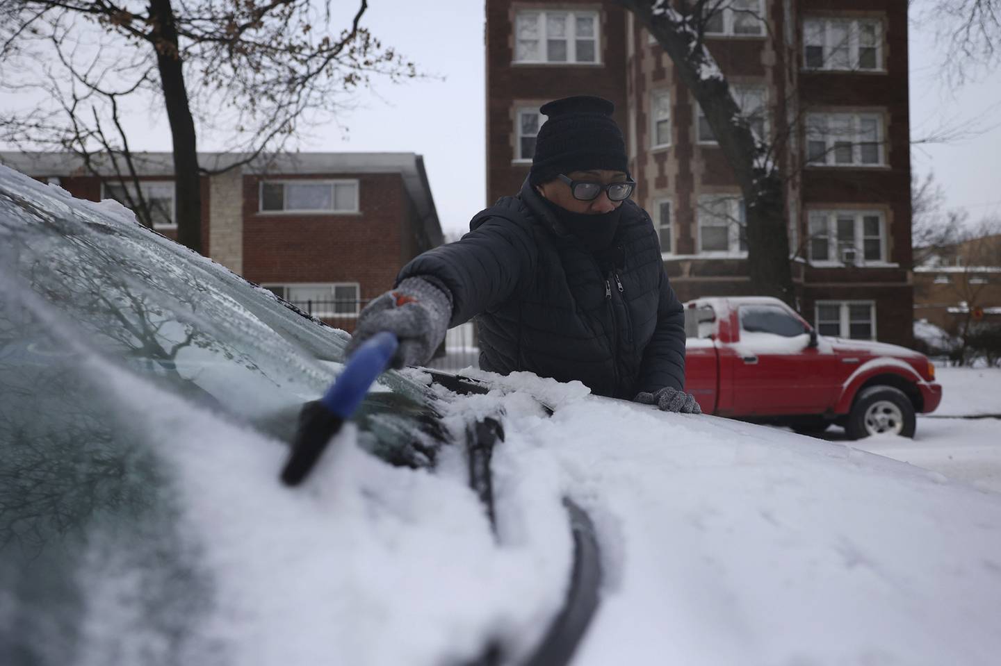 Arnida Edmonson wipes snow from her car in the below freezing temperatures on Dec. 23, 2022, in Chicago.