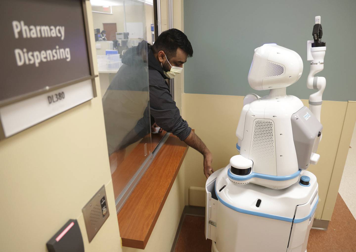 Aly Vishram, a pharmacy tech, places supplies in the drawer of Moxi the robot, one of two robots working at Elmhurst Hospital, on Dec. 1, 2022. Moxi will then take the supplies to the infusion center. 