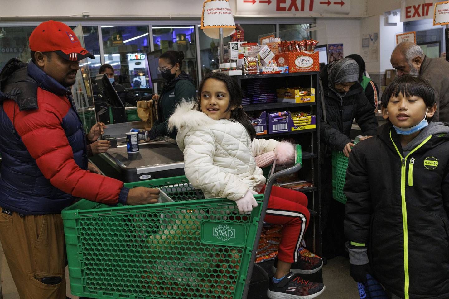Pawan Kumar Jha, left, unloads items while his daughter Krisha Jha, 7, sits in the basket as the family checks out at Patel Brothers grocery store in Chicago on Dec. 21, 2022, a day before a winter storm is expected to pass through the area.