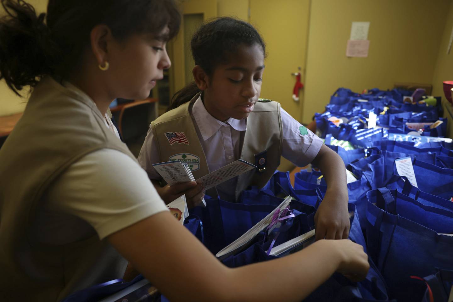 Girl Scouts Irene Vasquez, 12, left, and Jocelyn Vanzant, 12, put pamphlets in blue bags during a gift giveaway at the Pilsen Satellite Senior Center at Casa Maravilla on Dec. 18, 2022.