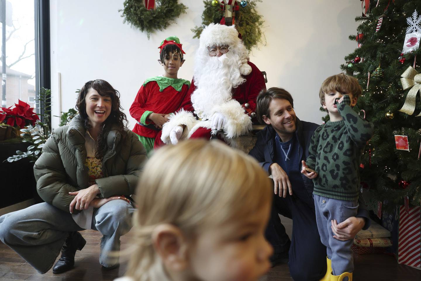 Santa Claus, played by Ronnie Trejo, waits for Sam Flores, 1, to pass before taking pictures with Katie Garvey, left, Santa's elf, played by Kamari Escobedo, 11, Ryan Ingebritson, and Ryan and Katie's son Artie, 3, at YO:U hair salon on Dec. 10, 2022, in Chicago. 