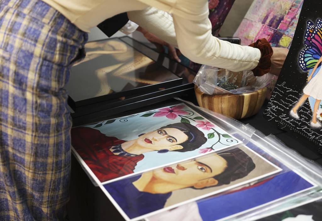 A worker arranges art pieces next to paintings depicting Mexican painter Frida Kahlo, created by mixed media artist Monserrat Moran, on display during a panel discussion about living as an immigrant with disabilities at the General Consulate of Mexico, March 23, 2023, in Chicago.