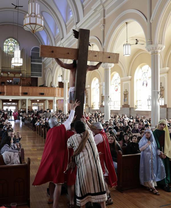 People playing Roman soldiers lift the cross holding Luis Gomez, playing the part of Jesus, inside Immaculate Conception Church on Chicago’s South Side on Good Friday, April 7, 2023.