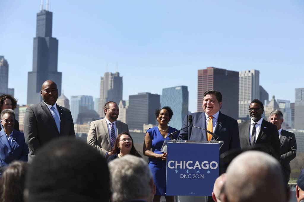 Dignitaries listen to Gov. J.B. Pritzker on a stage behind the Shedd Aquarium to celebrate the selection of Chicago as the host for the 2024 Democratic National Convention April 12, 2023. Behind Pritzker is Mayor-elect Brandon Johnson, right, and Democratic National Committee Chairman Jaime Harrison, left.