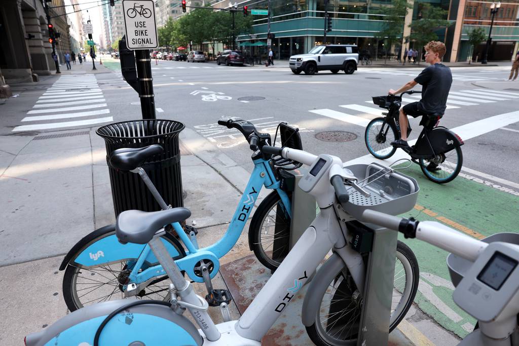 A Divvy bicycle rider waits for a light to change beside a Divvy station at Clinton and Washington in Chicago on June 22, 2023.