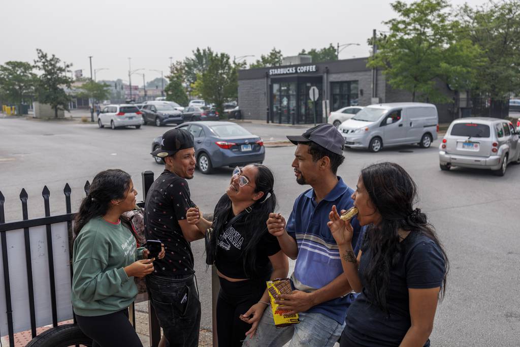 Alexa Ovalles, from left, Yorman Bravo, Julianna Ovalles, Alejandro Zavala, and Patricia Moyeja, all of Venezuela, eat near a fence while waiting for work in the Home Depot parking lot along West 87th Street  in Chicago on June 28, 2023.