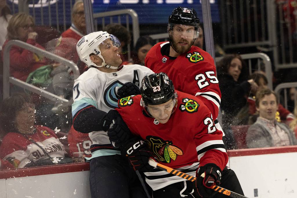 Blackhawks defenseman Jarred Tinordi (25) and center Philipp Kurashev (23) get tangled with Kraken center Jaden Schwartz on Oct. 23, 2022, at the United Center.