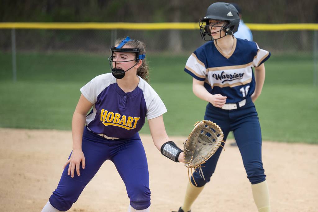 Hobart first baseman Alyssa Janik, left, holds Bishop Noll’s Kiera Quinlan during a game in Hobart on Wednesday, April 19, 2023.