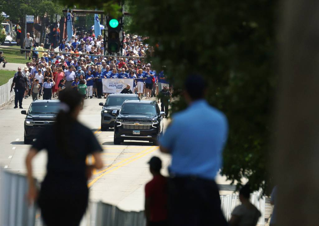 Police officers and neighbors line up to watch community members and politicians walk in honor of the victims and survivors of the Highland Park shooting on July 4, 2023.
