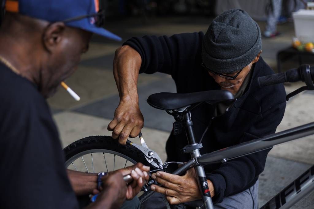 From right, Huberth Espinoza, 65, and Johnny Lloyd, 61, work on a bicycle Lloyd sold to Huberth outside the 5th District police station in Chicago on June 21, 2023.