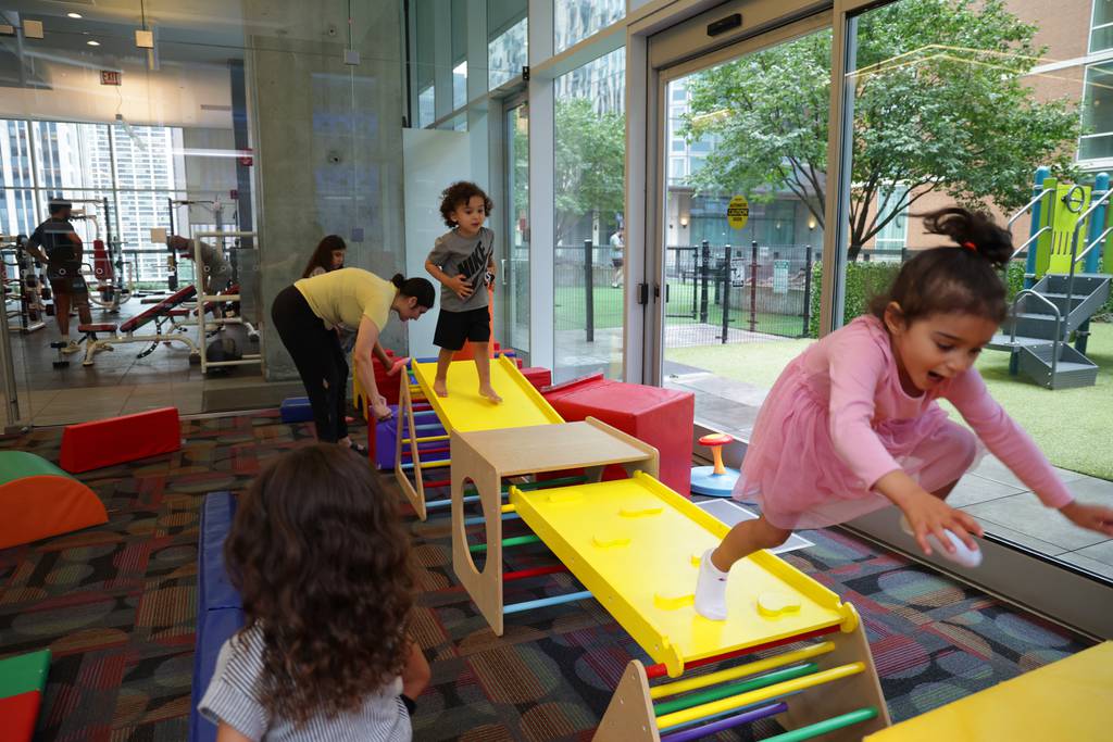 Two-year-old twins Dina, far right, and Zayn Matariyeh run across a play structure in the children’s playroom at the Optima Signature apartment building on Aug. 17, 2023, in Chicago. The building features many family-friendly amenities including indoor and outdoor play areas, two swimming pools and a Montessori school. 