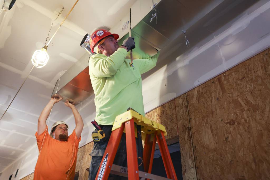 CJ Miller, left, and Tom Deneen install a trunk line for an HVAC system that will supply fresh air in the Conservatory Apartments in Garfield Park on Aug. 2, 2023. The system reuses conditioned air for energy savings.