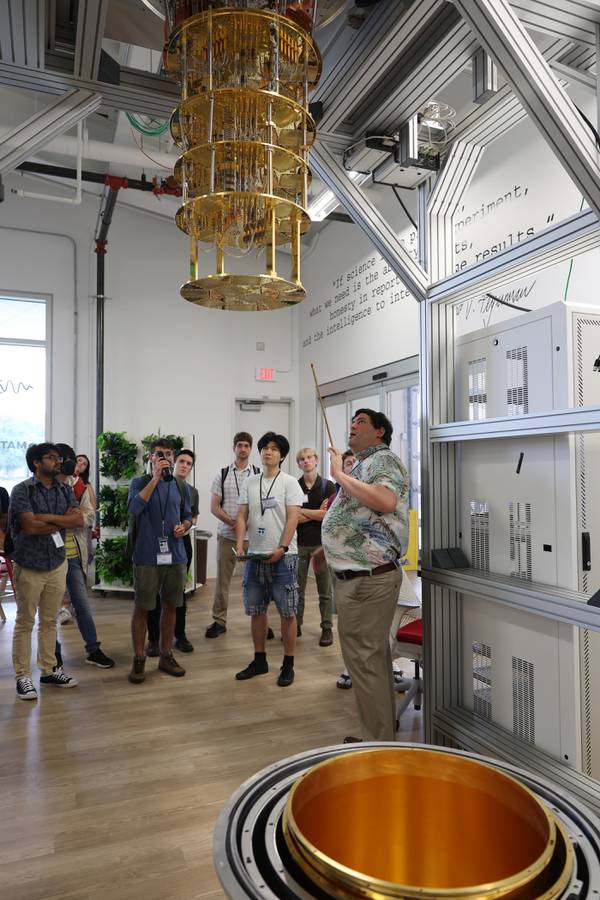 Matt Hollister points out details of a dilution refrigerator, a cryogenic device that provides continuous cooling, to students in the U.S. Quantum Information Science School program at Fermilab in Batavia on Aug. 9, 2023.