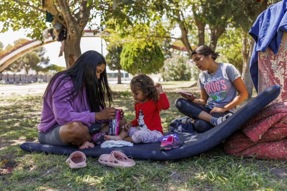 Luzmariany González Lerma, from left, her 3-year-old daughter Asumí Kataleya Ramírez González and Esthefania Vasquez Millán, all from Venezuela, wait in Chamizal Park in Ciudad Juárez, Mexico, to cross the border to El Paso, Texas, on July 12, 2023. Large groups of migrants live in the park while waiting to be notified if they can enter the U.S. using the CBP One app. 