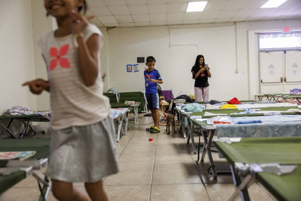 After eating dinner at the Holy Family Catholic Church migrant shelter, Yuledy, from left, Pedro and Yolexi pass the time before leaving for Denver July 13, 2023.