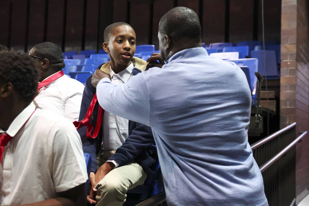 Staff member Joseph Jones helps sophomore Stephon Harden with his tie during the opening assembly on the first day of school at Urban Prep in Englewood on Aug. 21, 2023. 