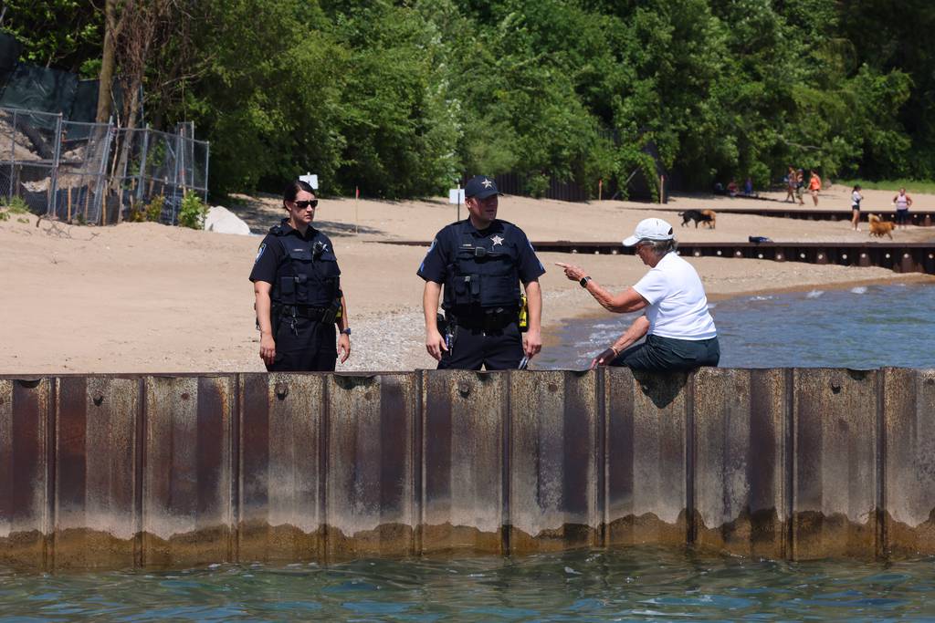 Mary Garrison, a former Winnetka Park District commissioner, right, sits on a seawall and chats with Winnetka police officers while watching construction on Justin Ishbia lakefront property in Winnetka on July 19, 2023. Since construction started earlier this summer, nearly all of the trees have been removed and the bluff has been taken down. The property was once home to three separate homes and is now a 3.7-acre site. 