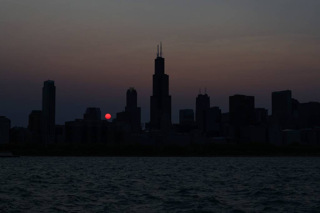 The sun sets behind the Chicago skyline, as seen from East Solidarity Drive on May 17, 2023, as smoke from Canadian wildfires dims the brightness of the sun.