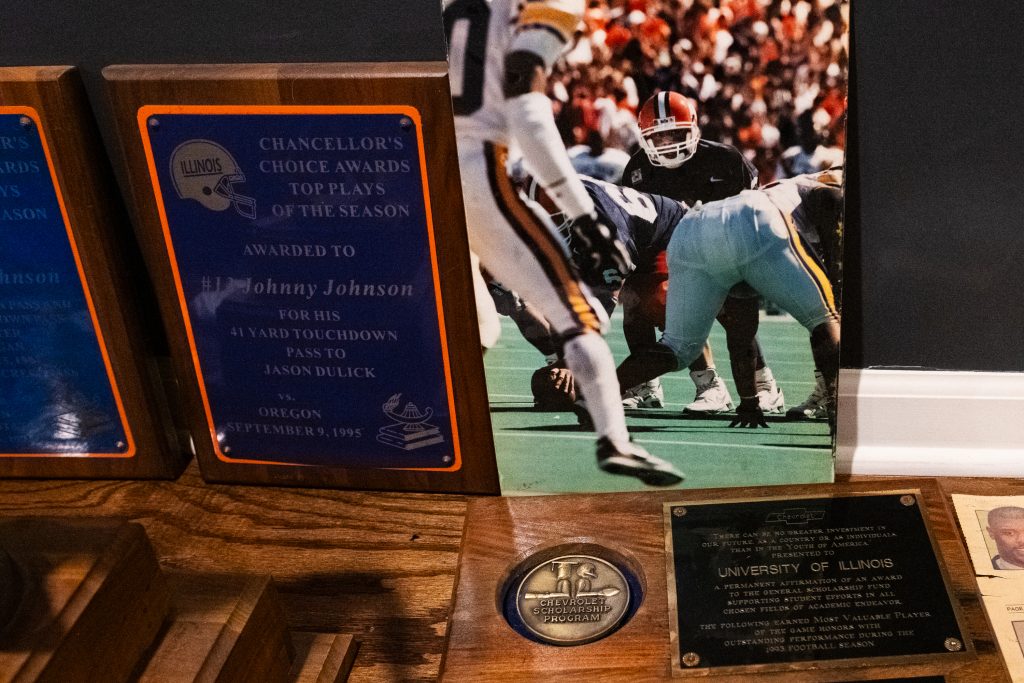 A photograph of Johnny Johnson, Jr. playing college football at the University of Illinois and his achievement awards shown in his home